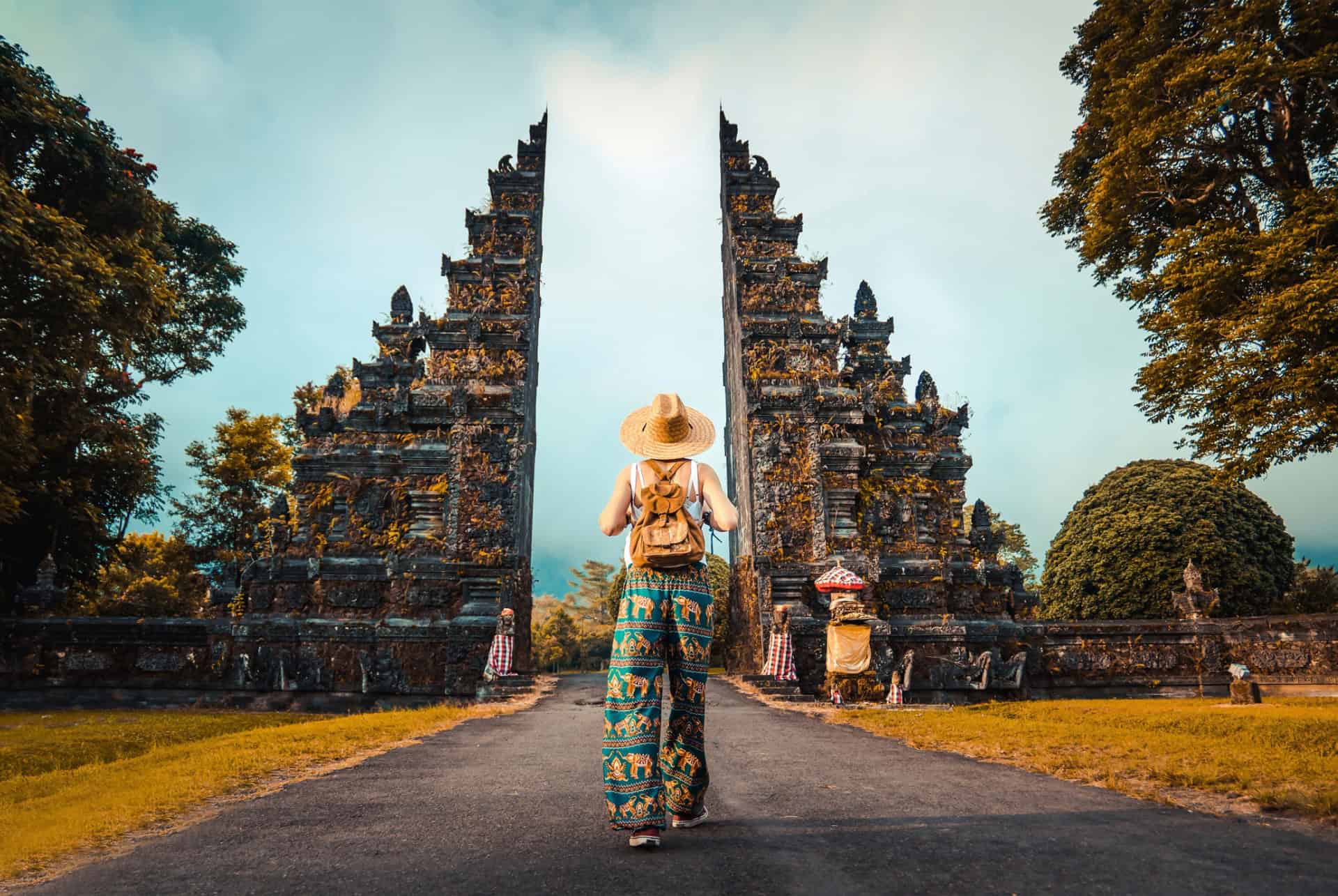 Voyageuse au chapeau de paille devant une porte de temple balinaise