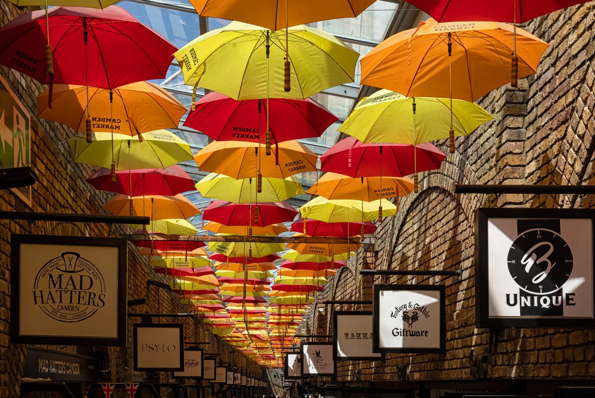 Allée de The Stables Market couverte de parapluies rouges, jaunes et orange sous une verrière